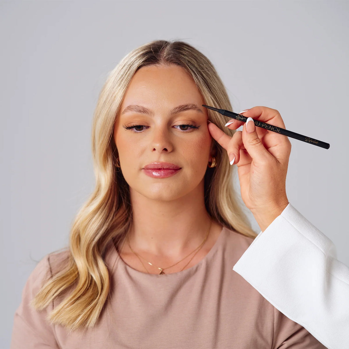 Professional artist using the Definitude Brow Pencil to shape a woman’s eyebrows, demonstrating precise PMU brow mapping on a neutral background.