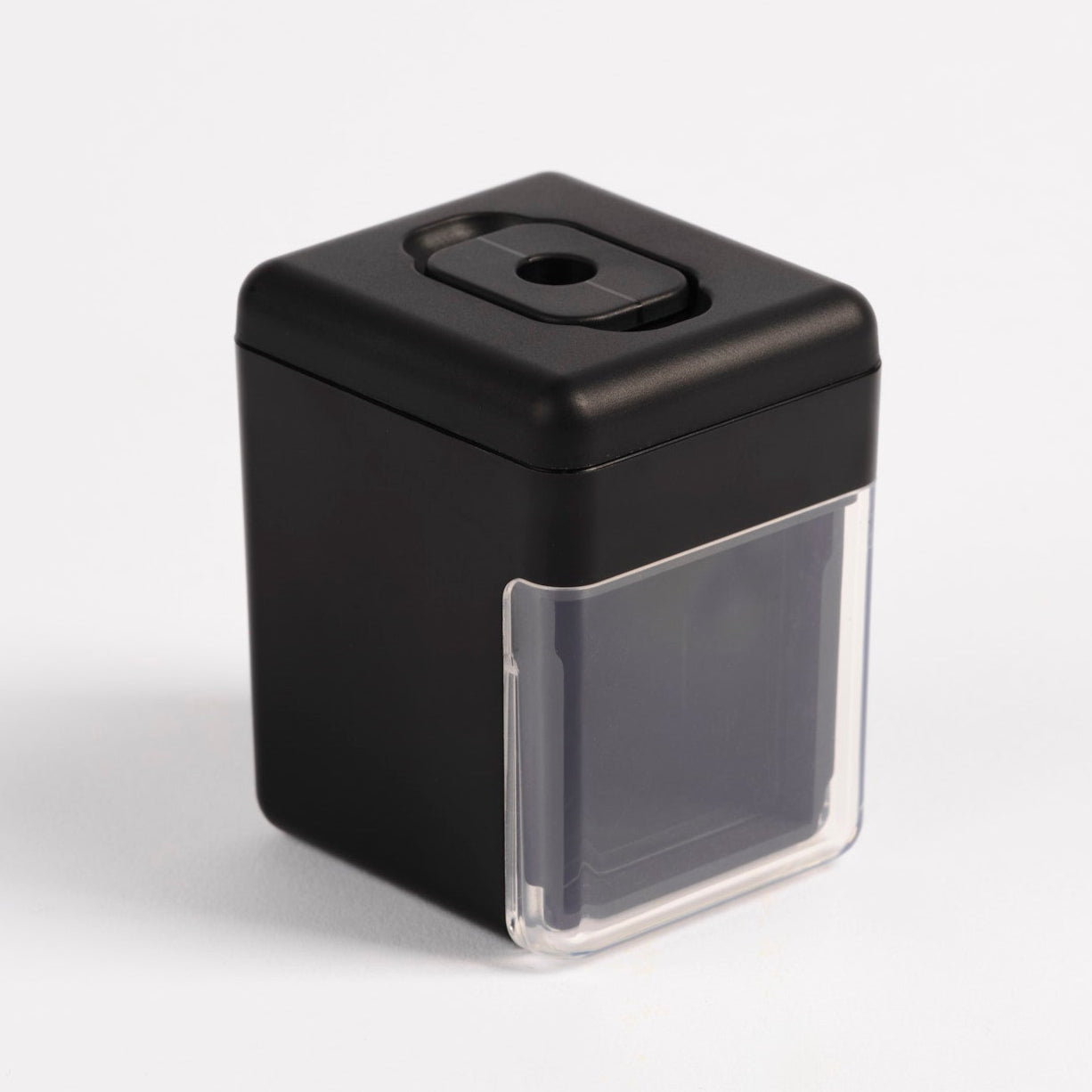 Angled view of the Pendulum PMU pencil sharpener featuring a clear waste container and matte black top, used for permanent makeup pencils.