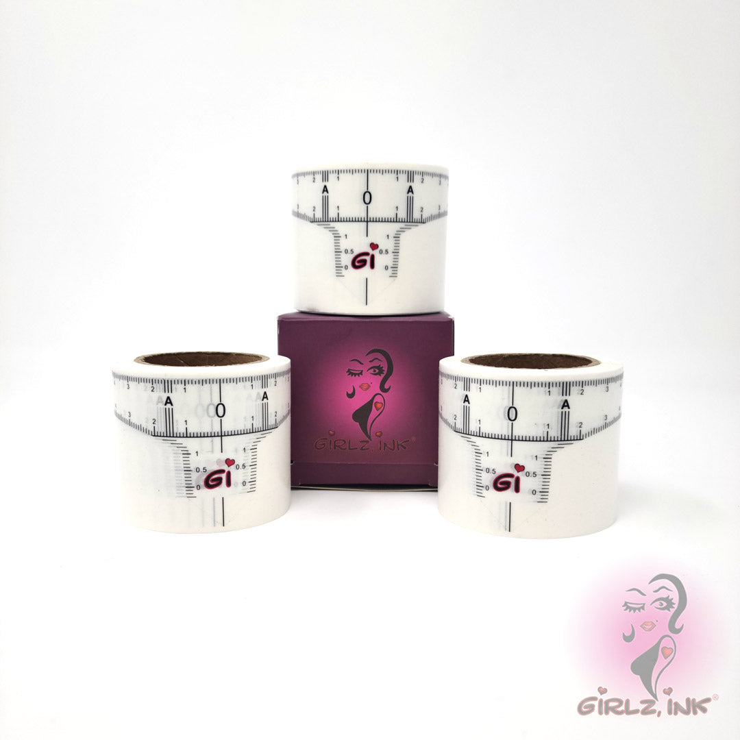 Girlz Ink disposable brow mapping ruler tape rolls displayed around a purple Girlz Ink box. White adhesive measurement tape marked with brow symmetry guides and the GI logo. Used by professional PMU artists for accurate eyebrow mapping, balanced measurements, and precise pre-draw.
